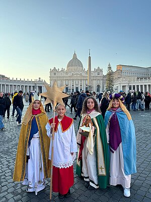 Zwei Mädchen und zwei Jungs stehen in Sternsingerkleidung auf dem Petersplatz in Rom. Zwei Mädchen und zwei Jungs stehen in Sternsingerkleidung auf dem Petersplatz in Rom.