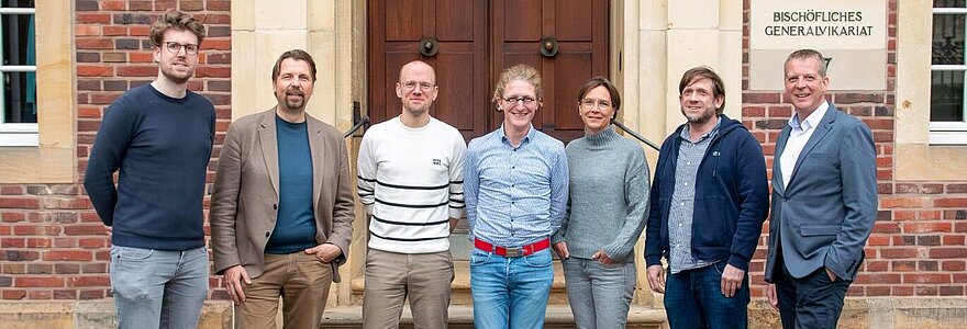 Martin Schroer, Matthias Mamot, Dr. Laurenz Wilken,  Daniel Gewand, Gudrun Niewöhner, Marcus Bleimann und Frank Mönkediek stehen vor dem Eingang des Bischöflichen Generalvikariates Münster.