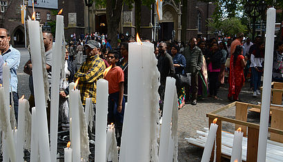 Im Vordergrund brennen viele Kerzen unterschiedlicher Größe, dahinter stehen Tamilen vor der Basilika in Kevelaer.