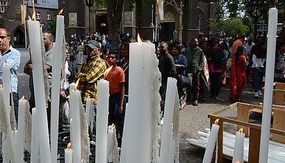 Im Vordergrund brennen viele Kerzen unterschiedlicher Größe, dahinter stehen Tamilen vor der Basilika in Kevelaer.