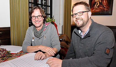Elmar Lehnen und Bastian Rütten (v.l.) sitzen an einem Tisch, vor ihnen ausgebreitet liegen Notenblätter.