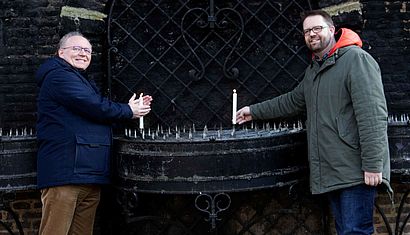Wallfahrtsrektor Gregor Kauling und Bastian Rütten stehen vor der Kerzenkapelle und haben jeweils eine Kerze in der Hand.
