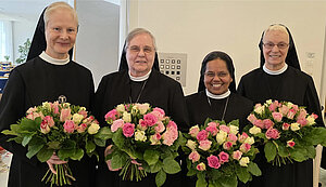 Vier Ordensfrauen in schwarzer Ordenskleidung und mit Blumensträußen in den Händen stehen nebeneinander. 