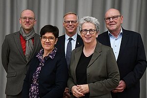 Dr. Laurenz Wilken, Jutta Loke, Dr. Klaus Winterkamp, Gisela Niehues und Günter Eilers stehen für ein Gruppenfoto vor einem grauen Vorhang. In der vorderen Reihe stehen zwei Frauen, beide mit kurzen Haaren und Brillen; sie lächeln in die Kamera. Hinter ihnen stehen drei Männer, ebenfalls lächelnd und formell gekleidet. 
