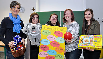 Die stellvertretende Schulleiterin und vier Schülerinnen halten Spielsachen und ein bunt bemaltes Plakat in die Kamera.