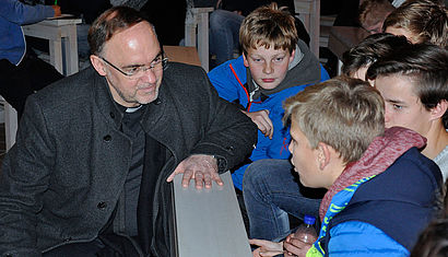 Weihbischof Rolf Lohmann sitzt in einer Kirchenbank und ist im Gespräch mit drei Jugendlichen.