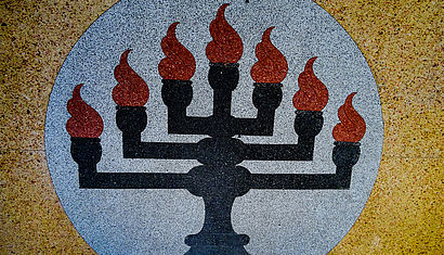 Auf Stein gemalter schwarzer, siebenarmiger Leuchter mit roten Flammen.