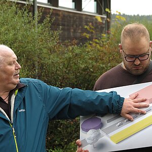 Ein Mann erklärt etwas und zeigt dabei auf einen 3D-Lageplan der Gedenkstätte Grafeneck. 