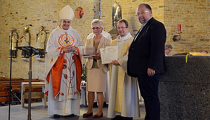 Bischof Genn überreicht eine Urkunde und eine Plakette. 