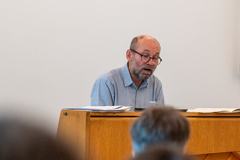 Der Chorleiter sitzt an einem kleinen, hölzernem Klavier.
