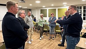 Drei Frauen und fünf Männer stehen beisammen und sprechen miteinander. Drei Frauen und fünf Männer stehen beisammen und sprechen miteinander.
