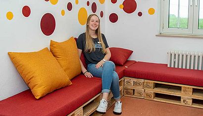 Eine junge Frau sitzt in einem Zimmer mit bunten Kreisen an der Wand.