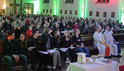 In der Christus-König-Kirche halten die Gemeindemitglieder rote und grüne Knicklichter in die Luft.