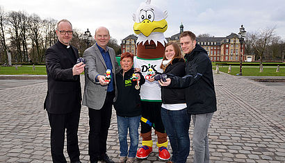 Vertreter des DJK-Sportverbandes stehen mit Dr. Stefan Vesper und Maskottchen "Carli" vor dem Münsteraner Schloss.
