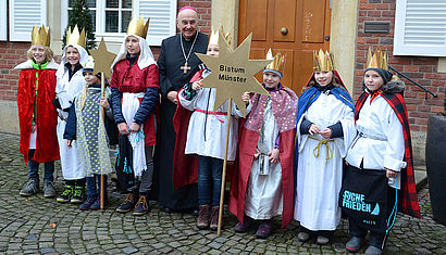 Acht als Sternsinger verkleidete Kinder stehen vor dem Bischofshaus in Münster, in ihrer Mitte steht Bischof Dr. Felix Genn. Ein Sternsinger trägt einen Stern mit der Aufschrift Bistum Münster.