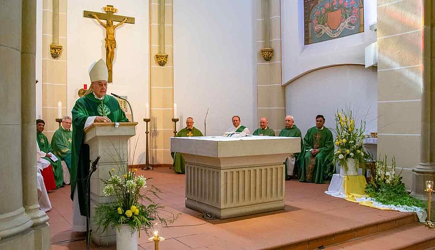 Im Altarraum einer Kirche steht links ein Bischof am Ambo und predigt.