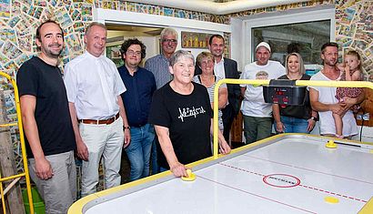 Zahlreiche Menschen stehen an einem Airhockey-Tisch.