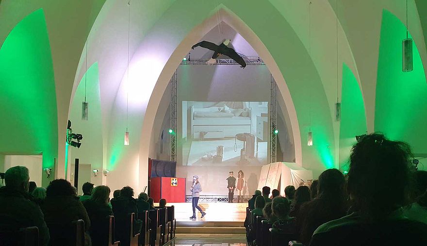 Blick von hinten in eine grün ausgeleuchtete Kirche, deren Altarraum zur Bühne umgebaut ist.