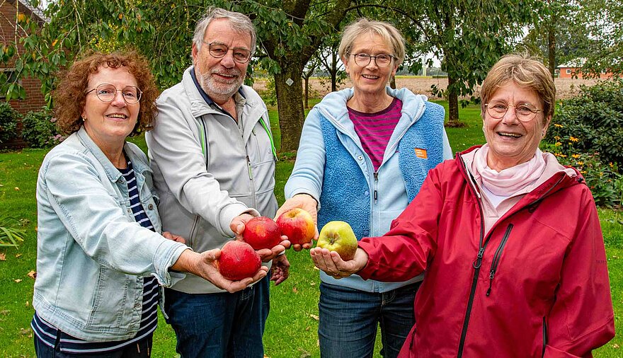 Drei Frauen und ein Mann stehen auf einer Obstwiese und halten jeweils einen Apfel in die Kamera. Drei Frauen und ein Mann stehen auf einer Obstwiese und halten jeweils einen Apfel in die Kamera.