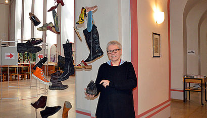 Künstlerin Ortrud Harhues steht vor ihrem Kunstwerk "Schuhwerk", viele Schuhe hängen von der Decke herab.