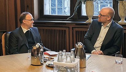 Weihbischof Rolf Lohmann und Oberbürgermeister Sören Link sitzen einander zugewandt an einem Tisch und sprechen miteinander.