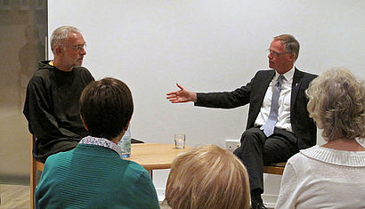 Vor Publikum sitzen links Bruder Paulus und rechts Generalvikar Dr. Klaus Winterkamp im Gespräch.