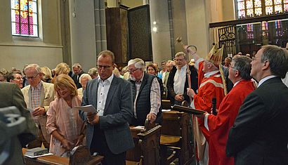 Im Mittelgang der vollen Kirche stehen Erzbischof Werner Thissen, der Weihwasser in Richtung des neuen Fensters sprengt, Pastor Alois van Doornick und Ministerpräsident Armin Laschet.