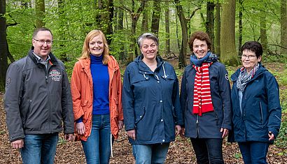 Vier Frauen und ein Mann stehen nebeneinander in einem Wald.