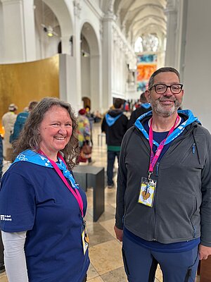 Eine Frau und ein Mann stehen lächelnd innen im Eingangsbereich eines großen, hellen Kirchengebäudes. Eine Frau und ein Mann stehen lächelnd innen im Eingangsbereich eines großen, hellen Kirchengebäudes.