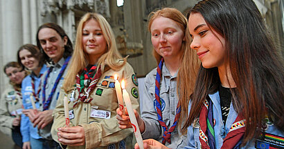 Das Bild zeigt sechs Pfadfinderinnen und Pfadfinder, die mit Stabkerzen das Friedenslicht weiterreichen. 