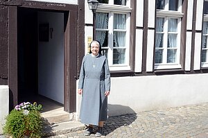 Schwester Maria Theodore Hofschen steht vor der Tür eines Fachwerkhauses.