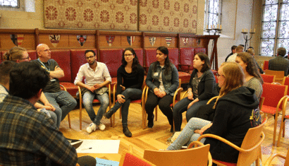 Eine kleine Gruppe von Menschen sitzt in einem Stuhlkreis zusammen