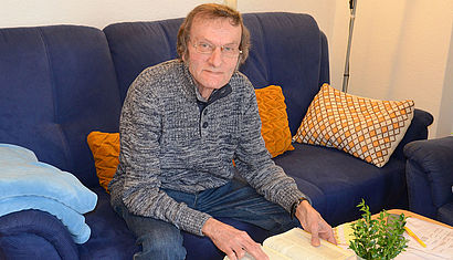 Klaus Höregott sitzt auf seinem Sofa und liest in der Bibel. 