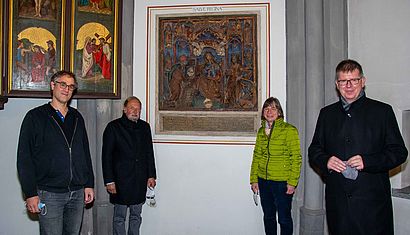 Eine Frau und drei Männer stehen vor einem Epitaph aus dem Mittelalter.