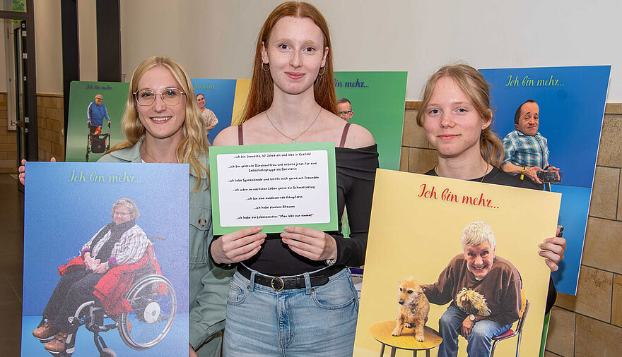 Drei Schülerinnern halten Plakate mit Fotos einer Ausstellung in den Händen.