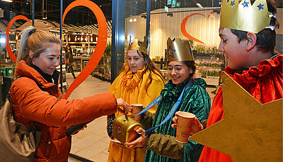 Sternsinger nehmen Spenden vor einem Supermarkt entgegen.