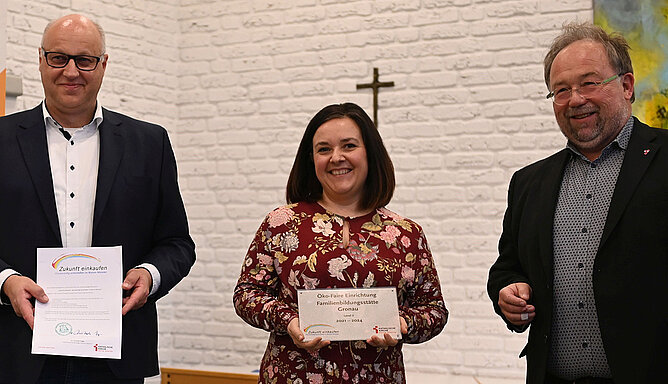 Thomas Kamp-Deister (rechts) überreicht die Plakette „Ökofaire Einrichtung nach Level 2“ an Diana Ricker (Mitte), Umweltbeauftragte der Familienbildungsstätte und Fachbereichsleiterin, und Fabi-Leiter Gerd Büscher. 