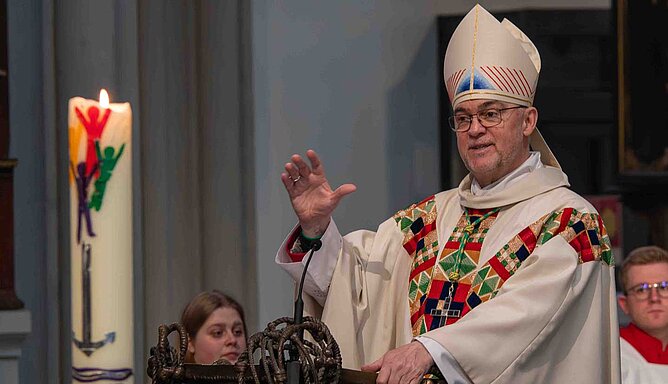 Weihbischof Lohmann steht am Ambo, vor ihm brennt eine Kerze mit dem Logo des Heiligen Jahres