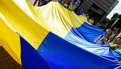 Teilnehmende der Demonstration tragen eine riesige Ukraine-Flagge vor sich her.