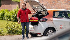 Markus Heitmann steht hinter einem weißen PKW des Caritasverband Ahaus-Vreden. Aus dem Kofferraum entnimmt er eine rote Tasche.eine Markus Heitmann steht hinter einem weißen PKW des Caritasverband Ahaus-Vreden. Aus dem Kofferraum entnimmt er eine rote Tasche.eine