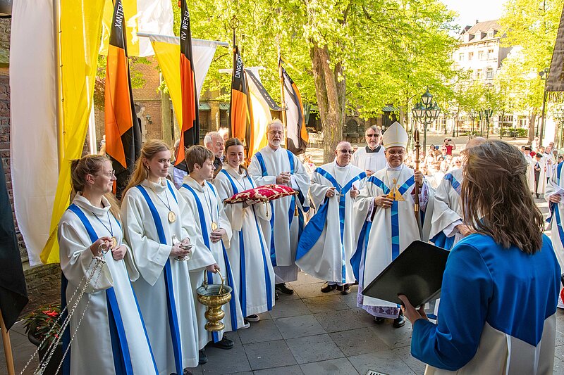 Ein Bischof sowie Messdiener und weitere Geistliche stehen auf den Stufen vor der Marienbasilika.