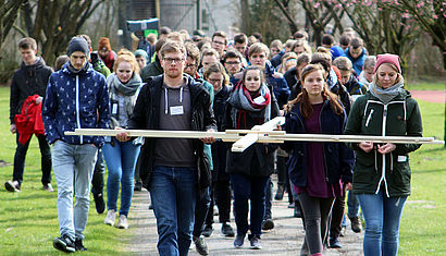 Junge Erwachsene tragen ein großes Kreuz durch die Natur. 