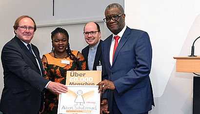 (v.l.) Dr. Stefan Oswald vom Bundesministerium für wirtschaftliche Zusammenarbeit und Entwicklung; Thérèse Mema Mapenzi, Leiterin Centre OLAME Bukavu, missio-Projektpartnerin; Pfarrer Dirk Bingener, Präsident missio Aachen; Dr. Denis Mukwege, Leiter Panzi-Hospital Bukavu und Träger des Friedensnobelpreises 2018 präsentieren eine Unterschriftenbox der Aktion Goldengel