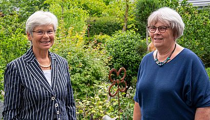 Zwei Frauen stehen mit Abstand zueinander in einem Garten.