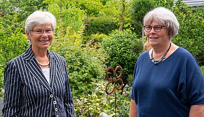 Zwei Frauen stehen mit Abstand zueinander in einem Garten.