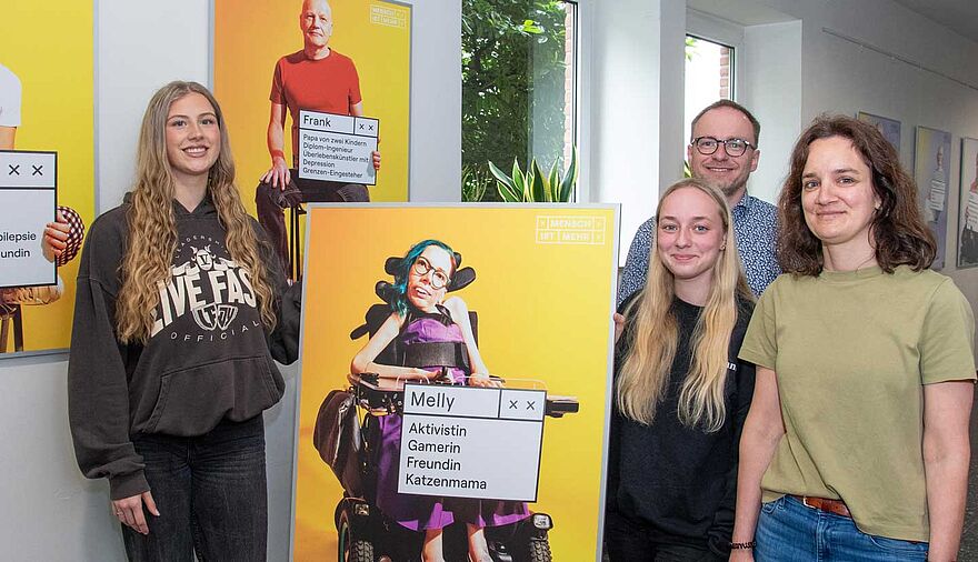 Zwei junge Frauen halten das Plakat einer Ausstellung, daneben stehen ein Mann und eine Frau.