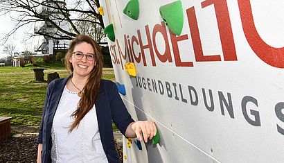 Sarah Kraschewski steht an einer Boulderwand, im Hintergrund ist der Michaelturm zu sehen.