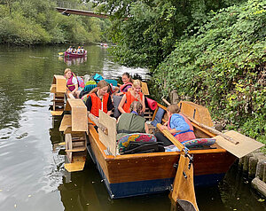 Jugendliche Mädchen mit Schwimmwesten sitzen in einem Tretboot auf einem Fluss. 