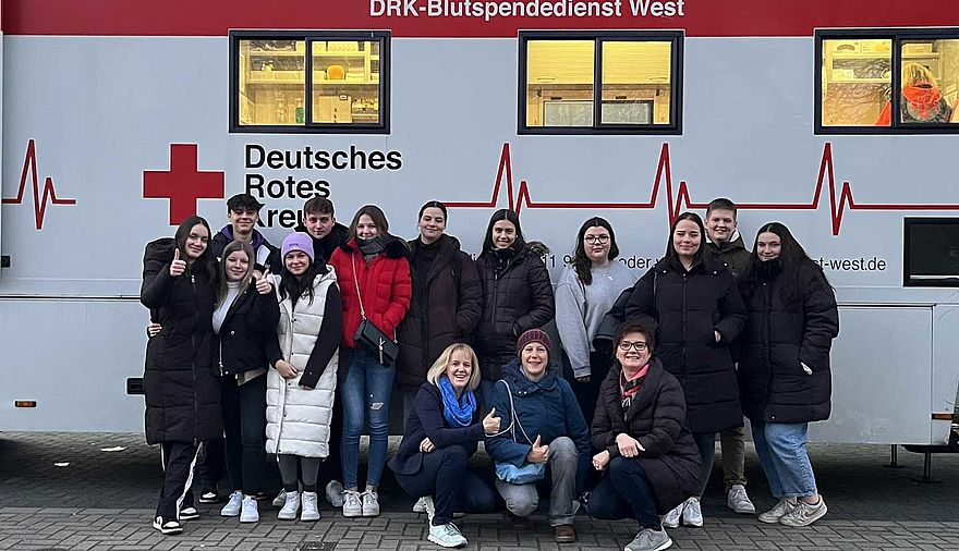 Junge Frauen und Männer stehen vor einem Blutspende-Bus des Deutschen Roten Kreuzes.