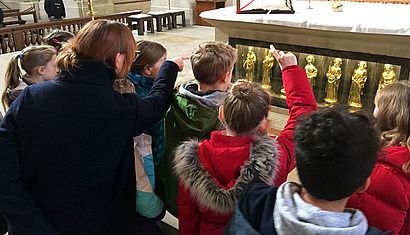 Kommunionkinder knien vor den goldenen Apostelleuchtern im Altar des St.-Paulus-Domes. 